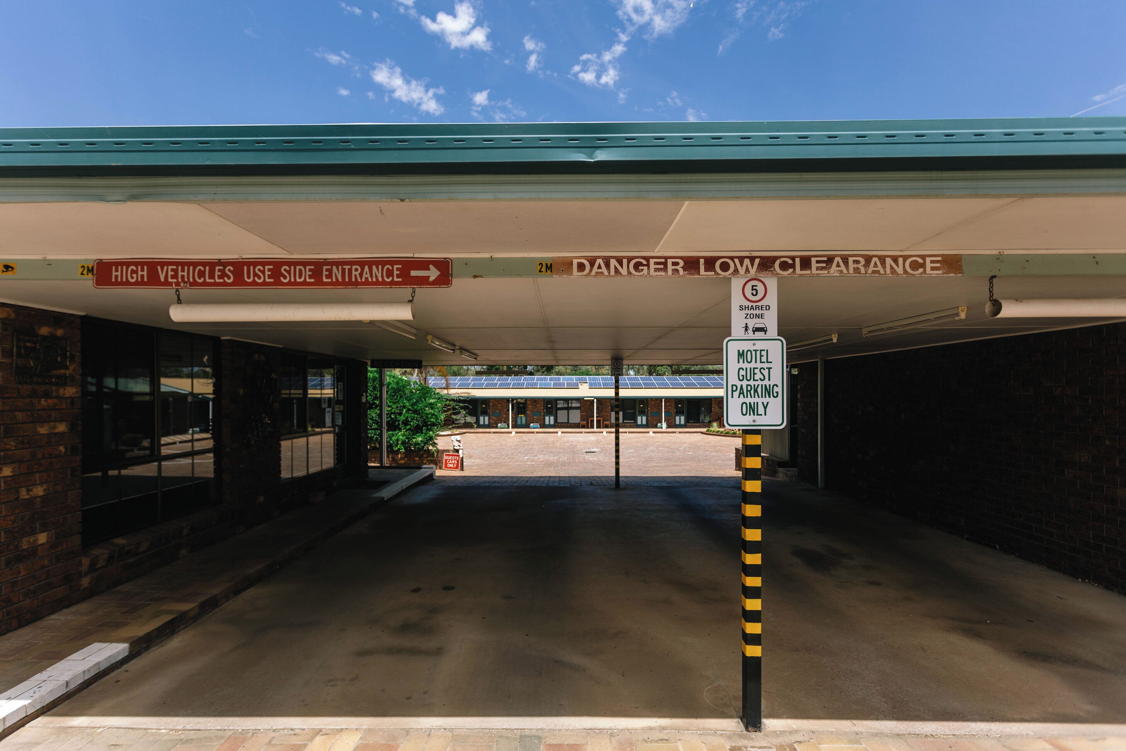 A hotel entrance with a sign indicating high vehicles use the side entrance and a warning for low clearance.