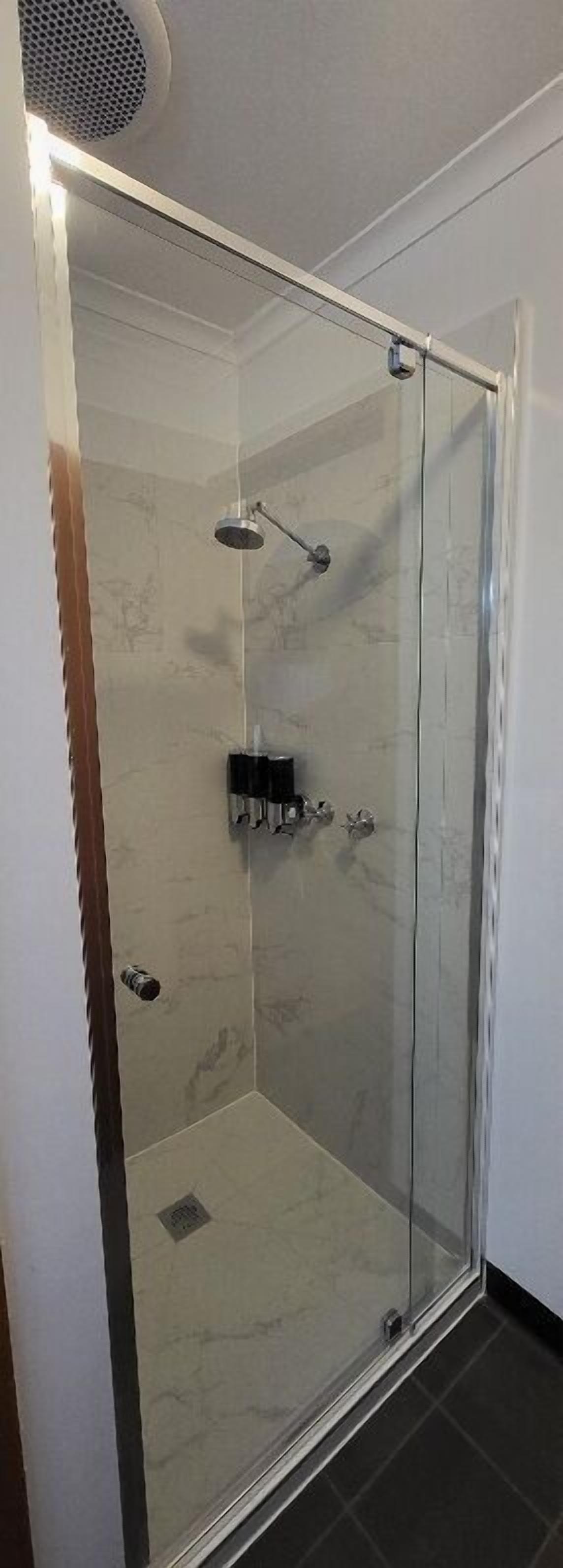 A glass-enclosed shower with a handheld showerhead and a wall-mounted control panel.