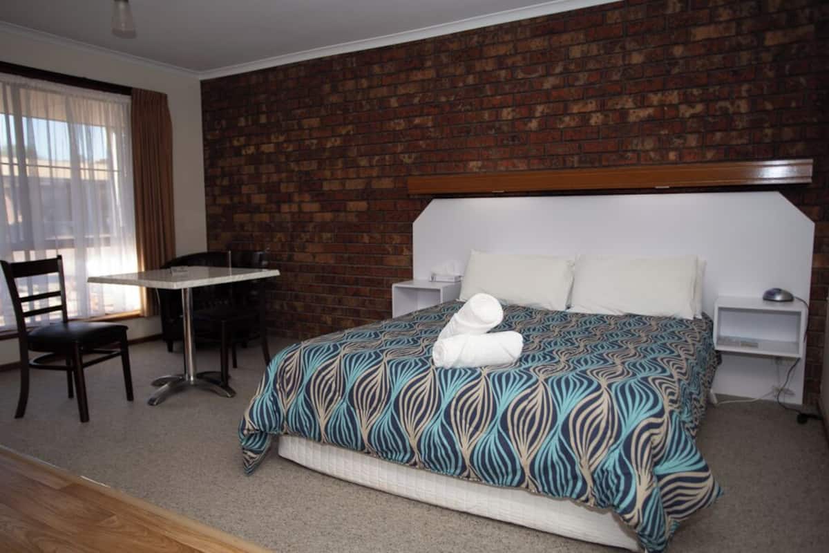 Une chambre d’hôtel avec un mur en briques, un lit recouvert d’une courtepointe à motifs, un bureau avec une chaise et une fenêtre avec des rideaux.