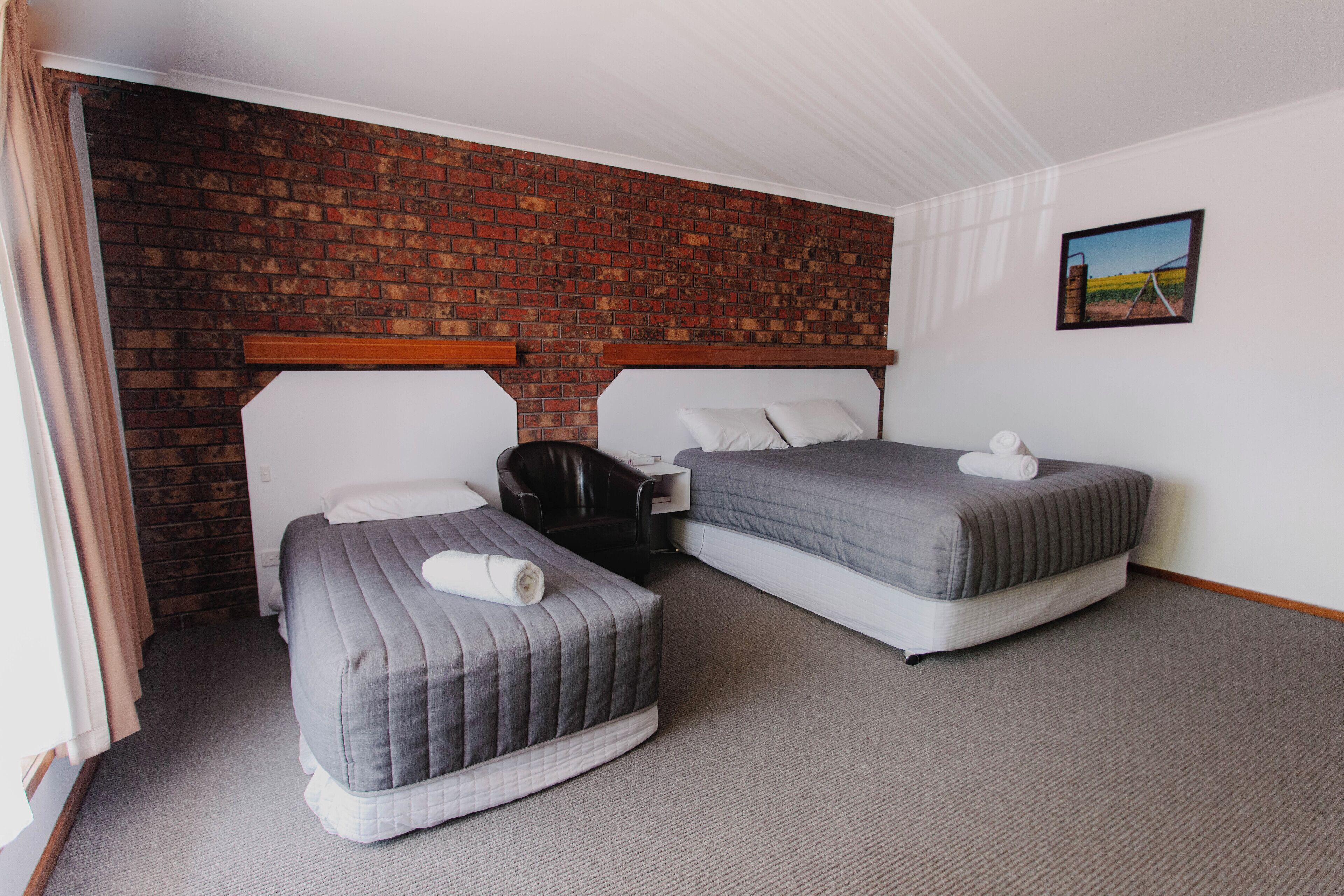 Ein Hotelzimmer mit zwei Betten, einer Backsteinwand und einem Bild an der Wand.