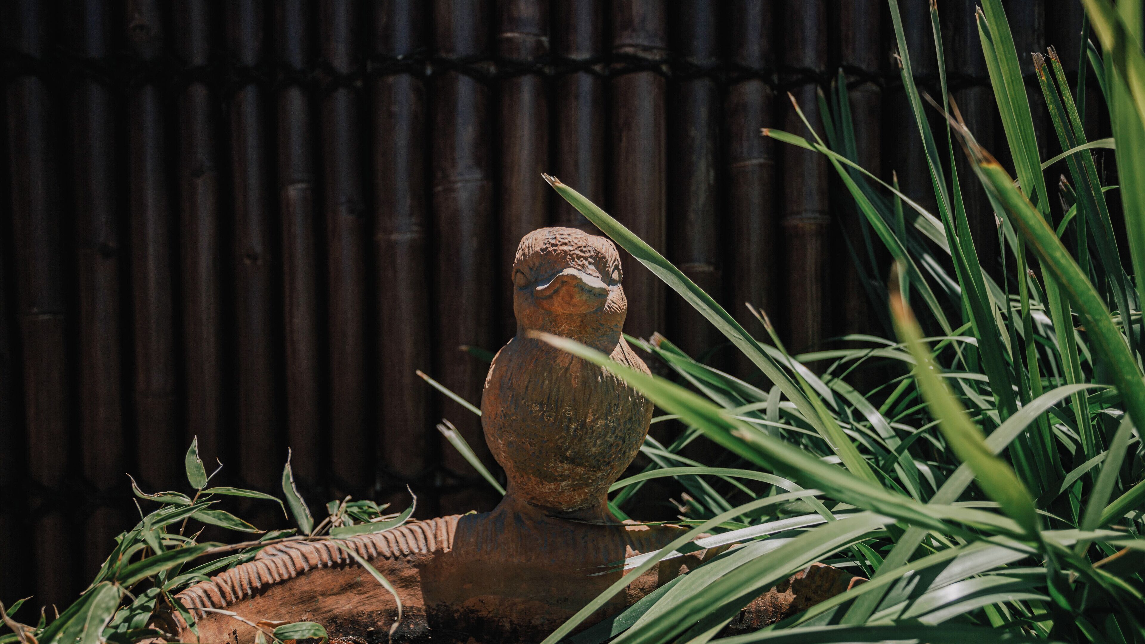 Una escultura rústica de pájaro rodeada de follaje.