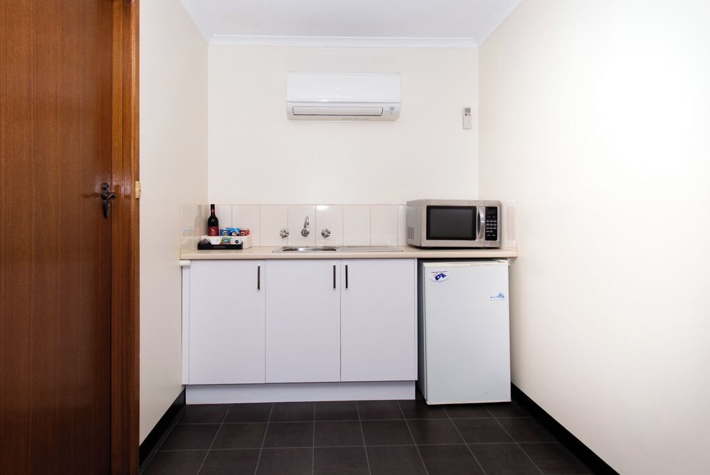 A compact kitchen with white cabinets, a microwave, a small refrigerator, and a sink.