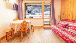 Una habitación acogedora con suelo de madera, una mesa de comedor con sillas, un sofá y un amplio ventanal con vistas a un paisaje nevado.