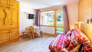 Una habitación acogedora con una cama, un armario de madera, una mesa de comedor con sillas y un televisor montado en la pared.