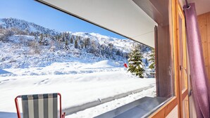 Vista desde una ventana: paisaje nevado, con una silla y una mesa de madera en una habitación.