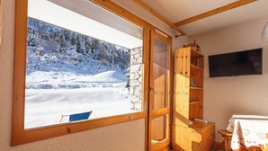 Une pièce dotée d’une grande fenêtre donnant sur un paysage enneigé, d’étagères en bois, d’un téléviseur et d’une table recouverte d’une nappe.