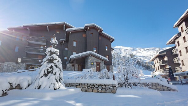 Un bâtiment enneigé, doté d’une façade en pierre et de nombreuses fenêtres, se dressant sur fond de montagnes recouvertes de neige.