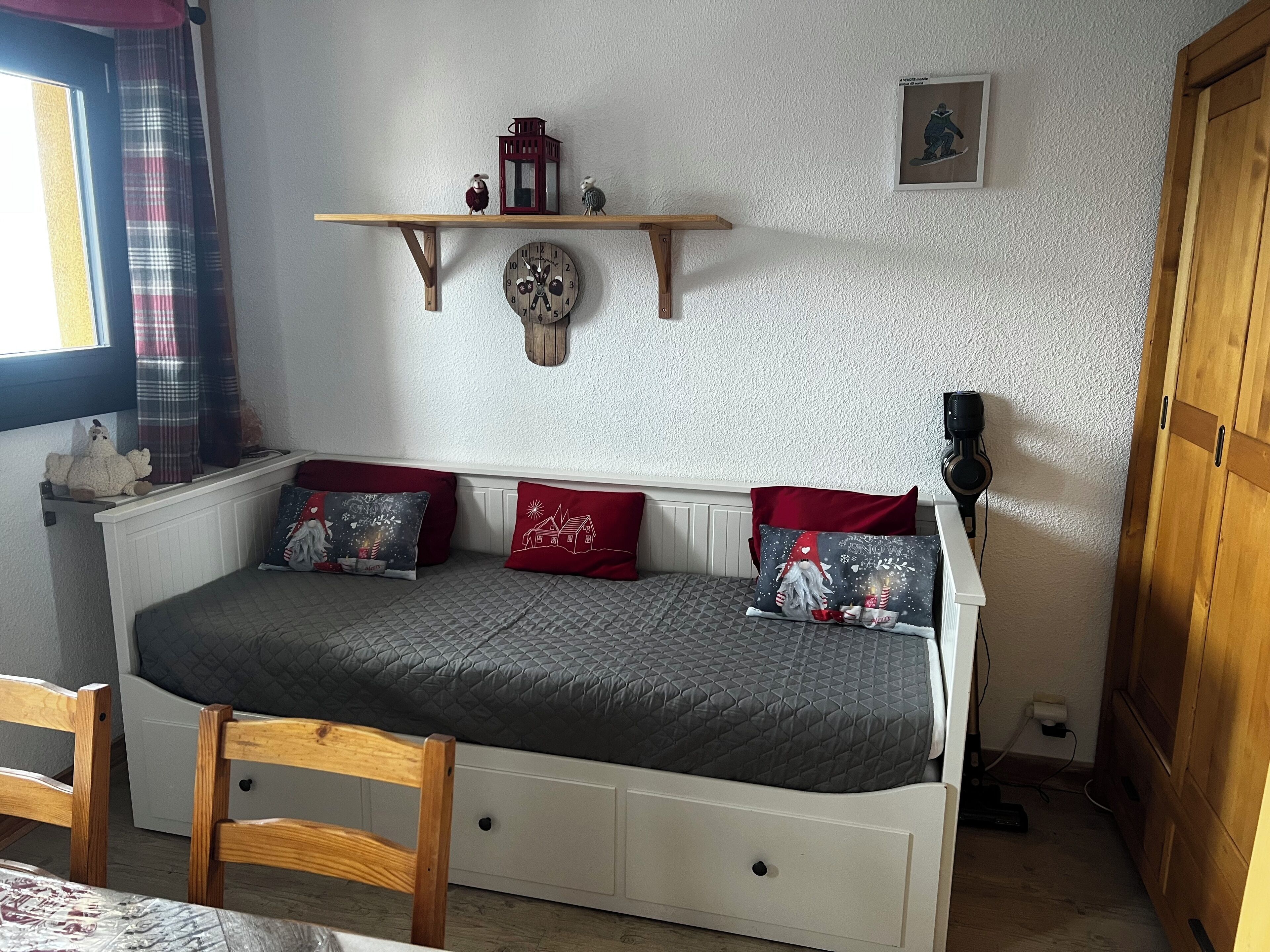 Una habitación acogedora con un sofá cama blanco, una silla de madera, una estantería con adornos y un reloj en la pared.