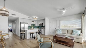 Una cocina moderna con armarios blancos, una isla central y un comedor con una mesa y sillas de madera.