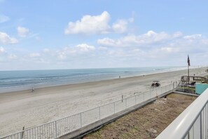 A beach view with a fence, a flag, and a distant person walking.