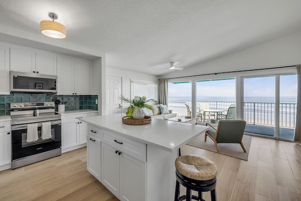 A modern kitchen with a central island, stainless steel appliances, and a view to the outside.
