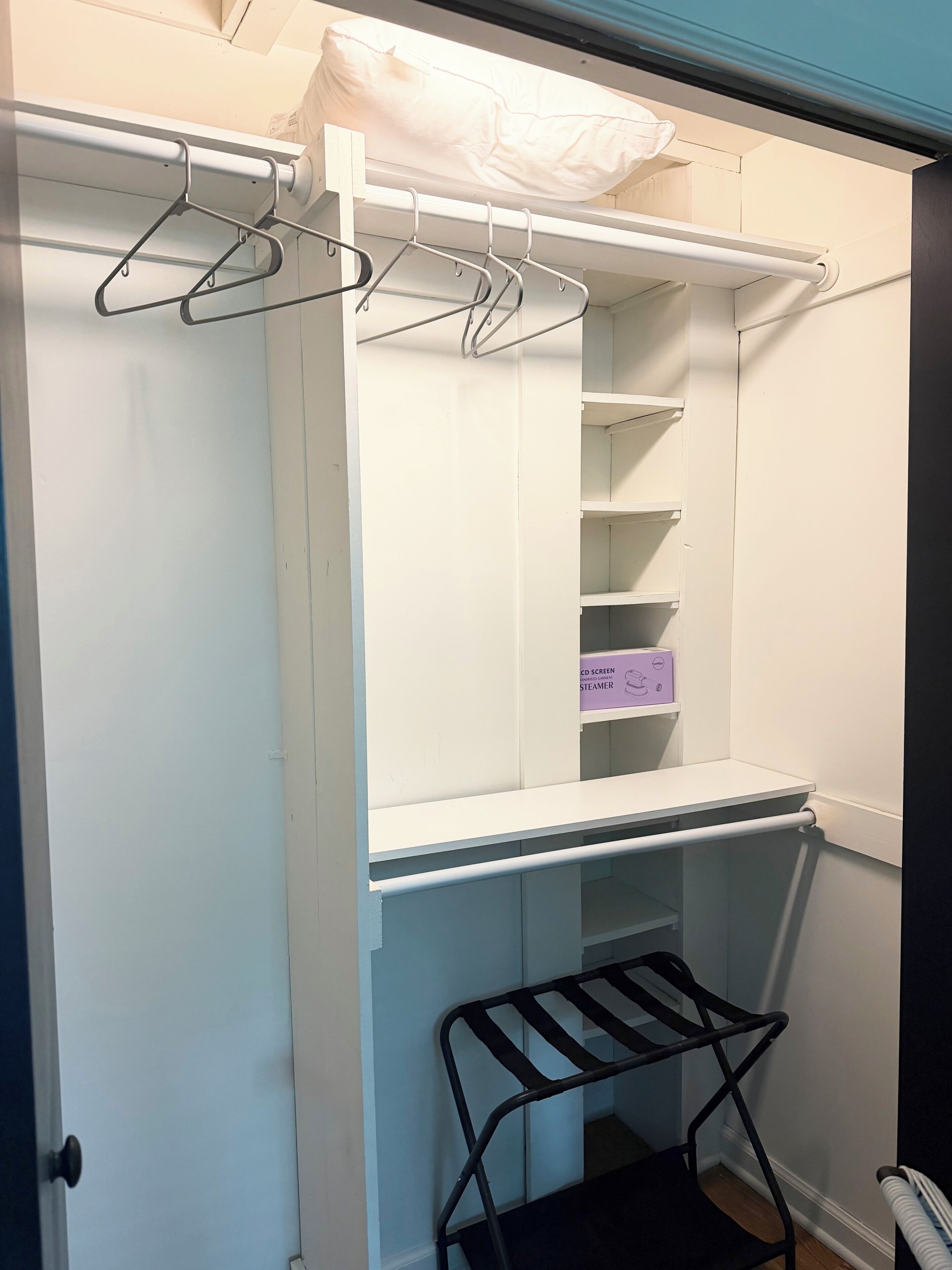 Un placard blanc avec des étagères, une tringle pour suspendre les vêtements et une chaise noire.