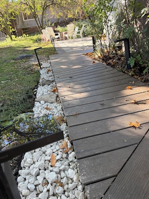 Un chemin en bois, bordé d’un côté de petits galets blancs, mène à du mobilier d’extérieur.