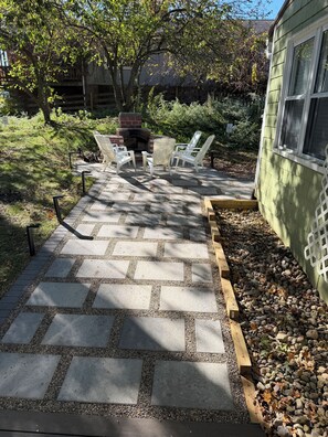 A patio with stone tiles, white chairs, and a brick fireplace.