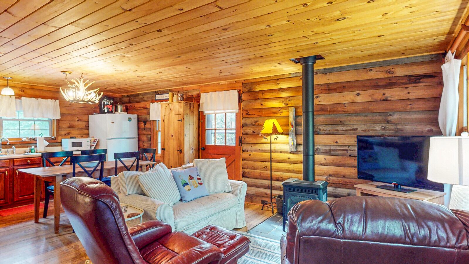 Un acogedor interior de cabaña con paredes de madera, una zona de comedor, un sofá, un televisor y una chimenea.