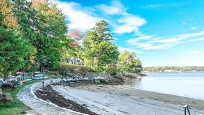 A stone pathway leading to a beach with a wooden fence and picnic tables.