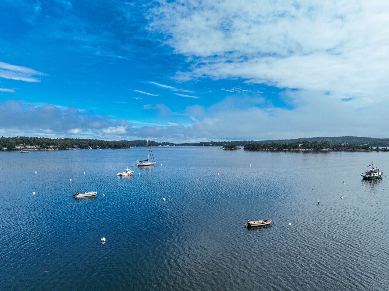A calm lake with several boats and buoys, surrounded by a forested shoreline.