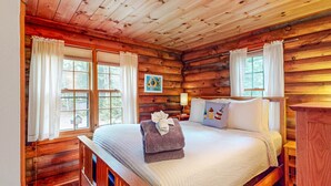 A wooden cabin bedroom with a bed, a nightstand, and a painting on the wall.