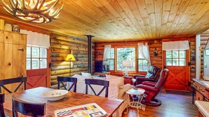 A log cabin interior with a dining area, a living room with a fireplace, and large windows.