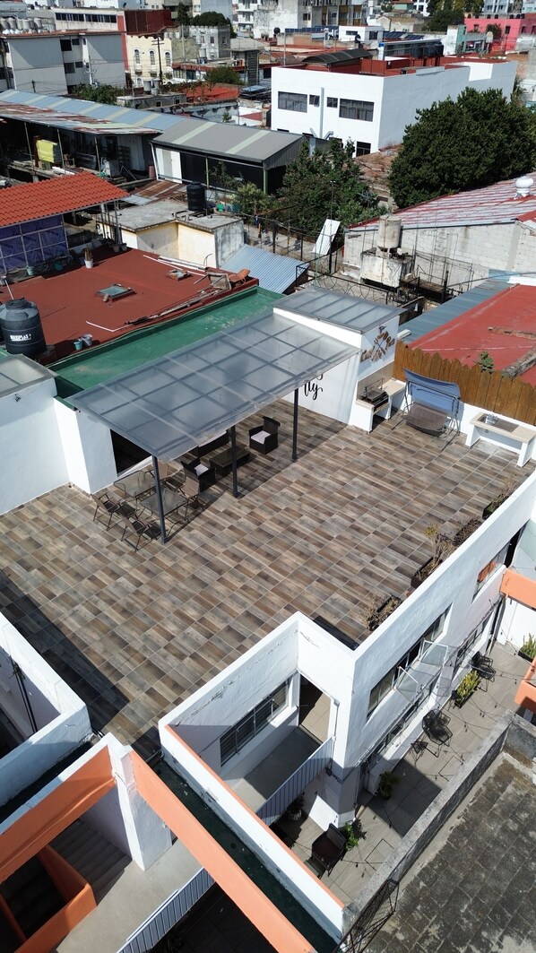Una azotea con un patio techado, piscina y vistas de edificios circundantes.