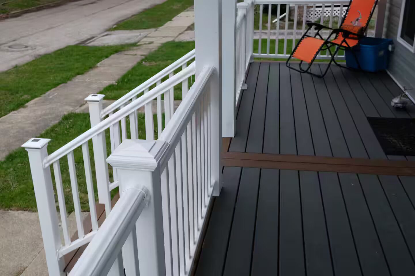 A wooden deck with white railings, a blue trash bin, and an orange chair.