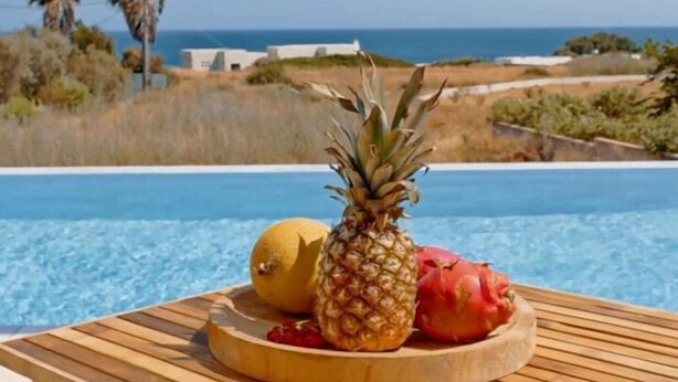 A wooden table with a fruit tray by a poolside, overlooking a beach and ocean. - Seadream Villa (Rhodes)