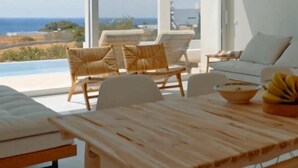 A modern living room with a wooden table, wicker chairs, and a view of the ocean. - Seadream Villa (Rhodes)