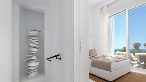 A modern bedroom with a large window, a bed with white bedding, and a unique wall-mounted bowl sculpture. - Seadream Villa (Rhodes)