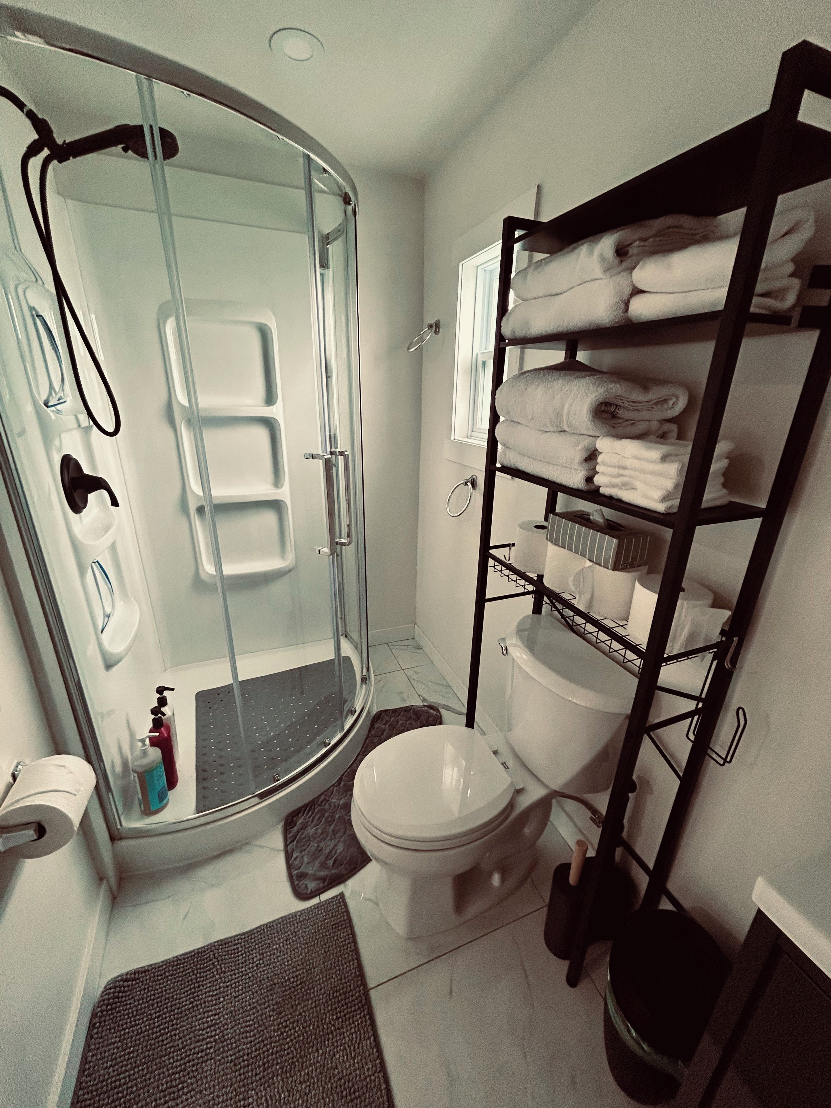 A bathroom with a glass-enclosed shower, a toilet, and a shelf with folded towels.