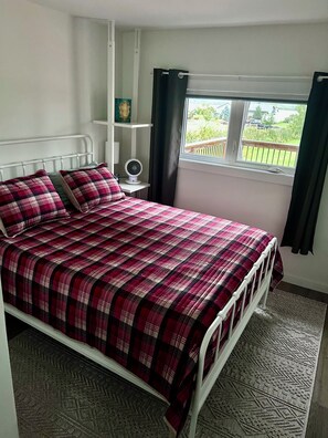 A bedroom with a bed, a bedside table, a fan, and a window with curtains.