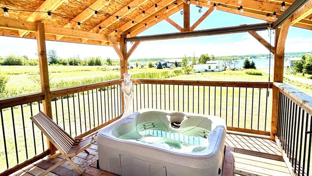 A wooden deck with a hot tub, wooden chairs, and a view of a lake and fields.