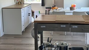 A modern kitchen with a central island, a dining area with a table and chairs, and a view of the outdoors through a large window.
