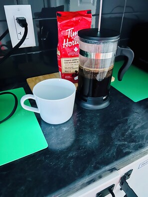 A coffee maker, a white mug, a green cutting board, and a Tim Hortons coffee bag on a kitchen counter. - Coastal Charm Meets Country Calm | Relaxing Cottage with Water Views & Hot Tub (Cocagne)