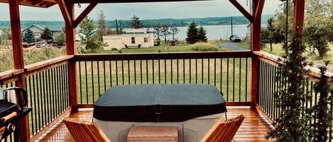 A covered outdoor seating area with a wooden deck, a table with chairs, and a view of a lake and buildings in the distance.