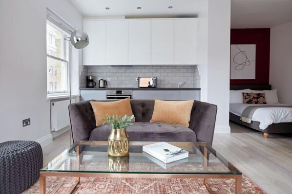 A modern living room with a glass coffee table, a grey sofa, and a red accent wall. - 6VH Virginia House, 31 Bloomsbury Way by City Living London (London)