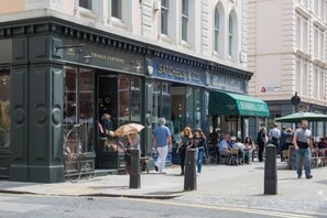 A street view of a cafe with outdoor seating, a bicycle parked outside, and pedestrians walking by. - 6VH Virginia House, 31 Bloomsbury Way by City Living London (London)