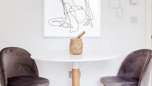 Ein moderner Essbereich mit zwei dunklen Stühlen, einem weißen Tisch und einem minimalistischen Kunstwerk darüber.