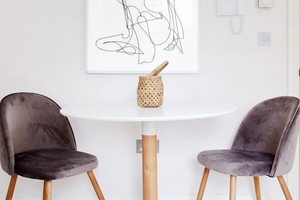 A modern dining area with two dark chairs, a white table, and a minimalist art piece above. - 6VH Virginia House, 31 Bloomsbury Way by City Living London (London)