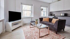Ein modernes Wohnzimmer mit einem Flachbildfernseher, einem Glastisch und einem dunklen Sofa.