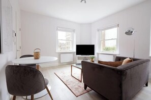 A modern living room with a sofa, a TV, and a dining area with a table and chairs. - 6VH Virginia House, 31 Bloomsbury Way by City Living London (London)