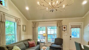 A living room with a chandelier, a sofa, a chair, a coffee table, and a dining area with chairs. - Charming 3-bedroom cottage in Historic McKinney, three blocks from the square. (McKinney)