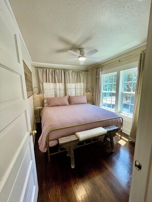 Un dormitorio con una cama, ventilador de techo, ventana con cortinas y una puerta.