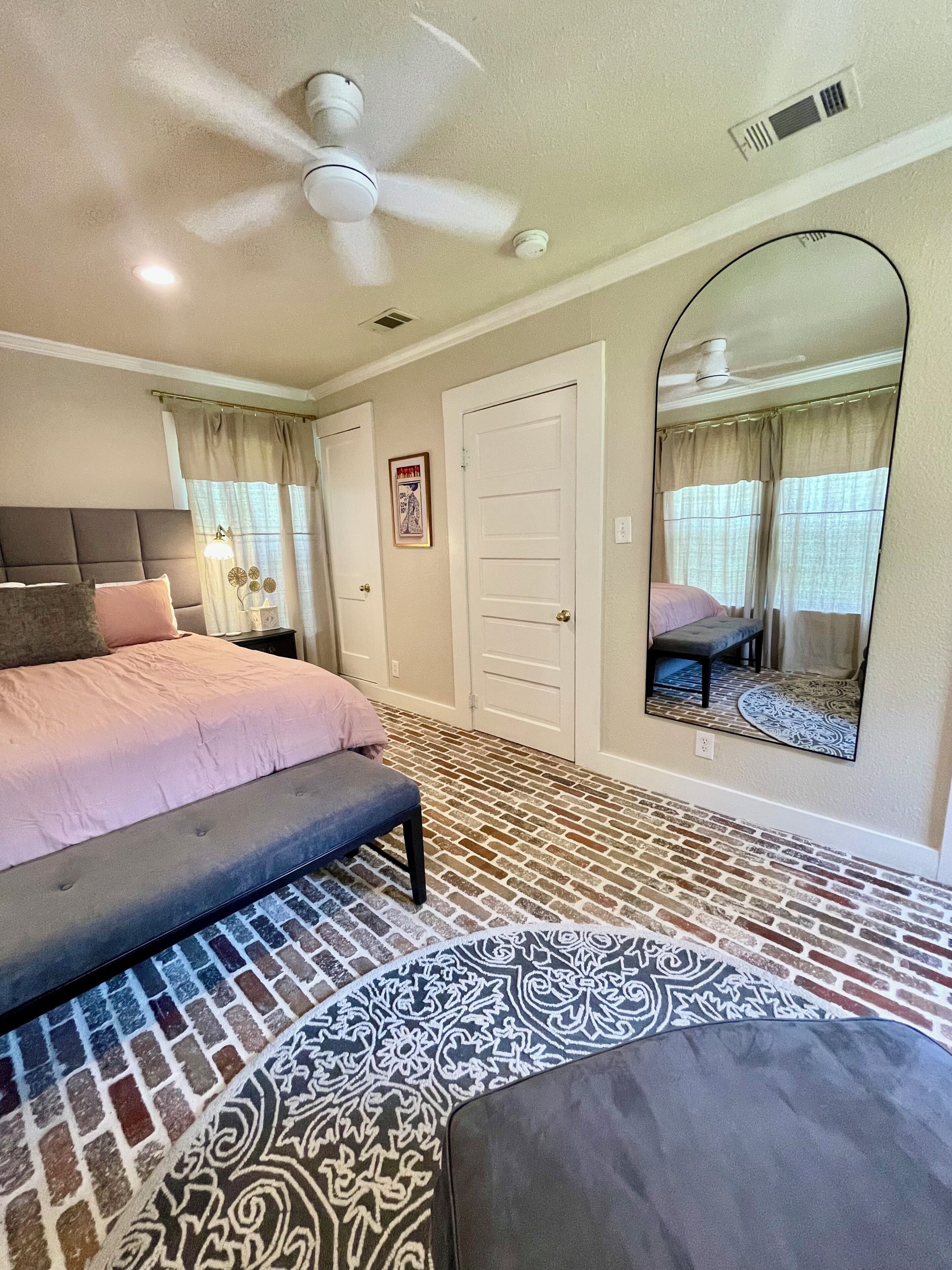 A bedroom with a bed, a bench, a ceiling fan, a door, and a mirror.