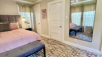 A bedroom with a bed, a bench, a ceiling fan, a door, and a mirror.