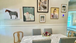 A dining area with a marble table, grey upholstered chairs, and artwork on the walls. - Charming 3-bedroom cottage in Historic McKinney, three blocks from the square. (McKinney)