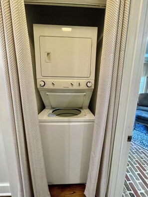 A compact, white laundry room with a front-loading washer and dryer, enclosed by beige curtains.