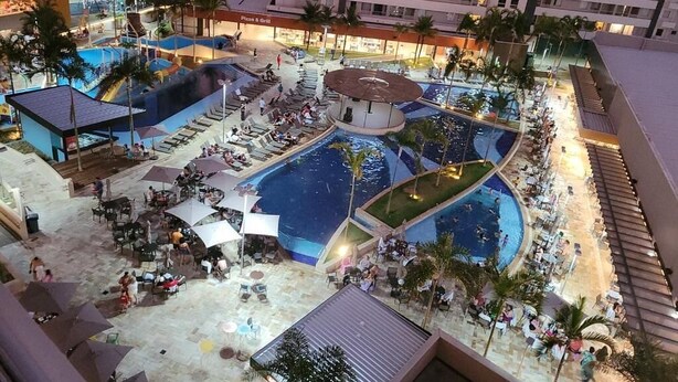 A resort with multiple swimming pools, outdoor seating areas, and a large building in the background. - Comfortable apartment for families with promotional price. (Olímpia)