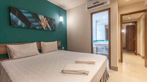 A hotel room with a large bed, a teal accent wall, a painting, an air conditioning unit, and a view of the bathroom and hallway. - Comfortable apartment for families with promotional price. (Olímpia)