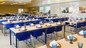 A large dining hall with multiple tables set for meals, blue chairs, and a buffet area in the background. - Comfortable apartment for families with promotional price. (Olímpia)