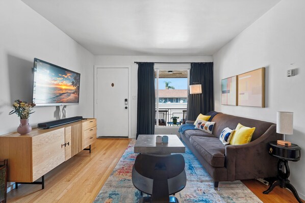 A modern living room with a sofa, coffee table, and TV. There is a view of the outside through a window.